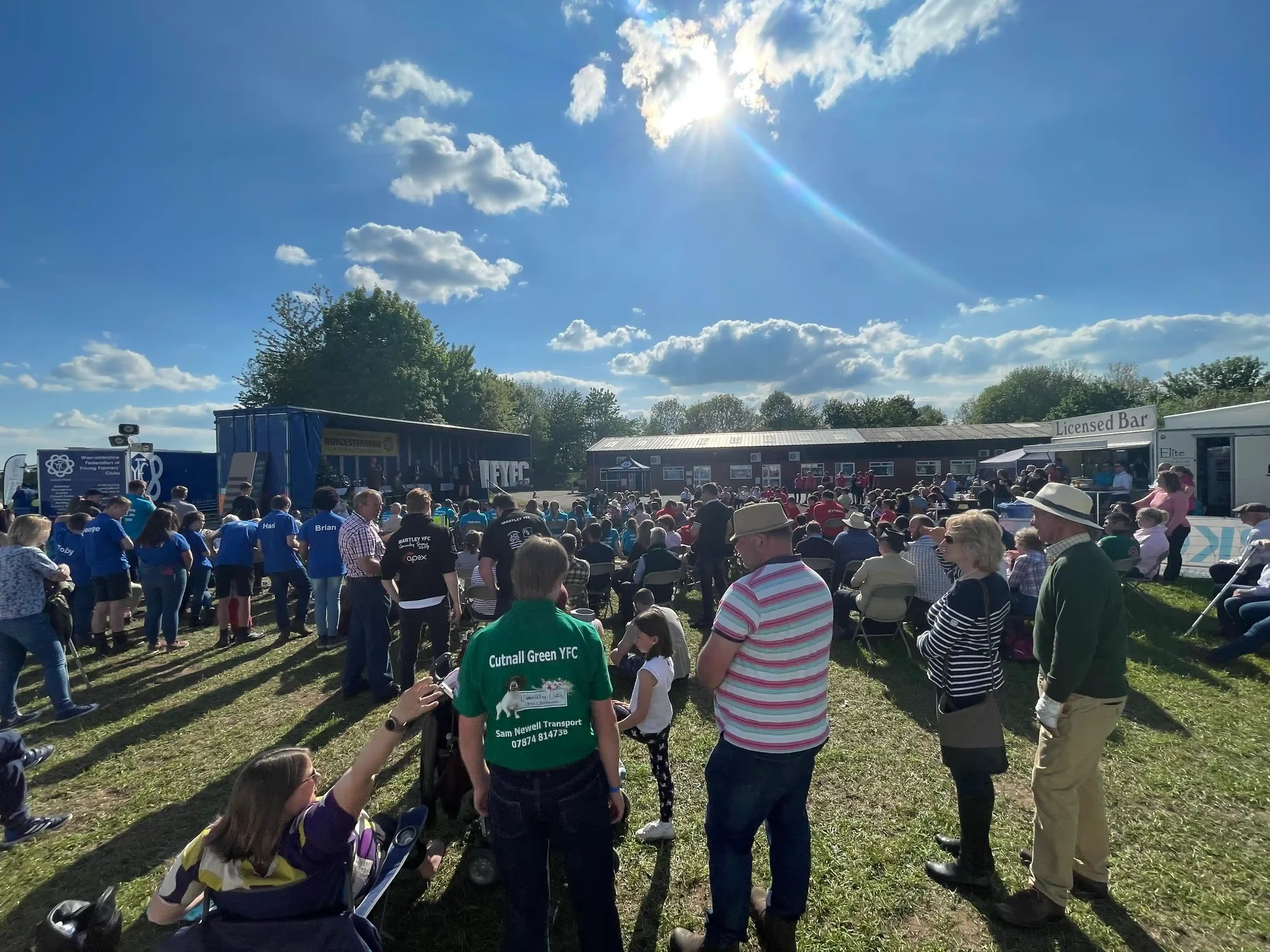 Members and public sat around stage listening to competition prize giving ceremony on hot sunny day